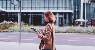 Şehirde yürüyen dijital tablet kullanan bir iş kadını. Yavaş hareket Gimbal dengelendi. İnternette kadın girişimci ağı, daktilo, mesaj, öğrenme, sabah ofise koşuşturma.