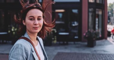 Şehirde yürüyen ve kamerayla konuşan genç bir kadın. Yavaş hareket, Gimbal Dengeleyici. İş kadını kameranın arkasındaki biriyle sohbet ediyor. Açık havada iletişim kurmak..