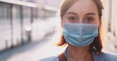 Şehirde koruyucu bir maske takan bir kadının portresi. Yavaş hareketli Gimbal Stabilizer atışı. Hava kirliliği ve Coronavirus covid-19 'a karşı maskeli genç bir kadın caddeyi geçiyor..