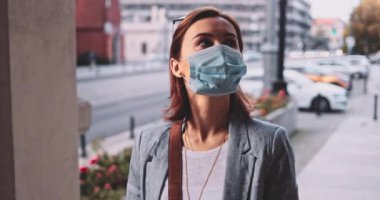 Şehirde koruyucu bir maske takan bir kadın. Yavaş hareket, Gimbal Dengeleyici. Hava kirliliği ve Coronavirus Covid-19 'a karşı maskeli genç bir kadın sokakta dolaşıyor. Şehir Sabahı.