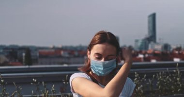 Nefes almak için tıbbi maskeyi çıkaran genç bir kadın. Yavaş hareket, Gimbal Dengeleyici. Kadın hava kirliliği ve koronavirüse karşı yüz maskesi çıkarıyor. Salgının sonu. Özgürlük, temiz hava.