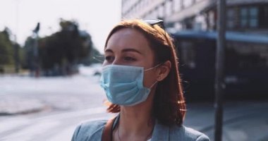 Koruyucu maskeli bir kadın kahve içiyor, şehirde yürüyor. Yavaş bir hareket yap. Genç bayan hava kirliliğine ve Coronavirus covid-19 'a karşı maskesini çıkararak kağıt bardaktan su içiyor..