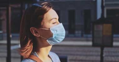 Şehirde koruyucu bir maske takan bir kadının portresi. Yavaş hareketli Gimbal Stabilizer atışı. Hava kirliliği ve Coronavirus covid-19 'a karşı maskeli genç bir kadın caddeyi geçiyor..