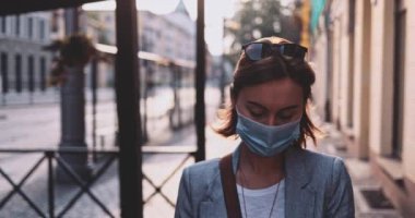 Şehirde koruyucu bir maske takan bir kadın. Yavaş hareket, Gimbal Dengeleyici. Hava kirliliği ve Coronavirus Covid-19 'a karşı maskeli genç bir kadın sokakta dolaşıyor. Şehir Sabahı.