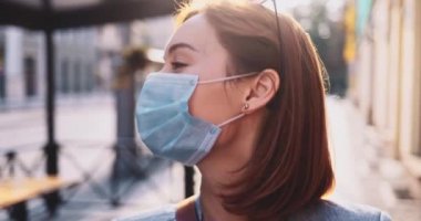 Şehirde koruyucu bir maske takan bir kadının portresi. Yavaş hareketli Gimbal Stabilizer atışı. Hava kirliliği ve Coronavirus covid-19 'a karşı maskeli genç bir kadın caddeyi geçiyor..