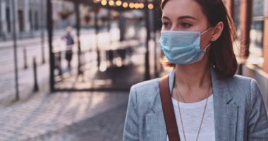 Şehirde koruyucu bir maske takan bir kadın. Yavaş hareket, Gimbal Dengeleyici. Hava kirliliği ve Coronavirus Covid-19 'a karşı maskeli genç bir kadın sokakta dolaşıyor. Şehir Sabahı.