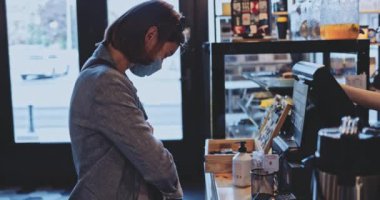 Koruyucu Maskeli Kadın Kahve Dükkanı 'ndan sipariş veriyor. Yavaş hareket, dengeleyici. Hava kirliliği ve Coronavirus 'a karşı maskeli bir iş kadını, kahveye erişimi olmayan bir kredi kartıyla para ödüyor..