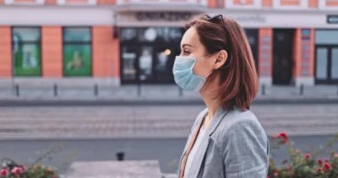 Şehirde koruyucu bir maske takan bir kadın. Yavaş hareket, Gimbal Dengeleyici. Hava kirliliği ve Coronavirus Covid-19 'a karşı maskeli genç bir kadın sokakta dolaşıyor. Şehir Sabahı.