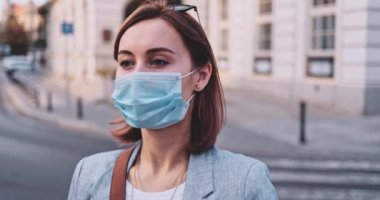 Şehirde koruyucu bir maske takan bir kadının portresi. Yavaş hareketli Gimbal Stabilizer atışı. Hava kirliliği ve Coronavirus covid-19 'a karşı maskeli genç bir kadın caddeyi geçiyor..