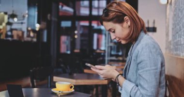 Bir kafede akıllı telefon kullanan genç bir kadın. Yavaş hareket, dengeleyici. Business Woman bir kafede sosyal medya için videolar çekiyor, iletişim kuruyor, kişisel markasını oluşturuyor, çevrimiçi. Hayatta teknoloji.