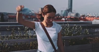 Nefes almak için tıbbi maskeyi çıkaran genç bir kadın. Yavaş hareket, Gimbal Dengeleyici. Kadın hava kirliliği ve koronavirüse karşı yüz maskesi çıkarıyor. Salgının sonu. Özgürlük, temiz hava.
