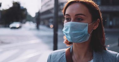 Koruyucu maskeli bir kadın kahve içiyor, şehirde yürüyor. Yavaş bir hareket yap. Genç bayan hava kirliliğine ve Coronavirus covid-19 'a karşı maskesini çıkararak kağıt bardaktan su içiyor..