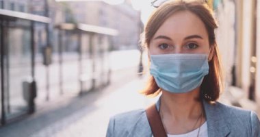 Şehirde koruyucu bir maske takan bir kadının portresi. Yavaş hareketli Gimbal Stabilizer atışı. Hava kirliliği ve Coronavirus covid-19 'a karşı maskeli genç bir kadın caddeyi geçiyor..