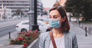 Şehirde koruyucu bir maske takan bir kadın. Yavaş hareket, Gimbal Dengeleyici. Hava kirliliği ve Coronavirus Covid-19 'a karşı maskeli genç bir kadın sokakta dolaşıyor. Şehir Sabahı.