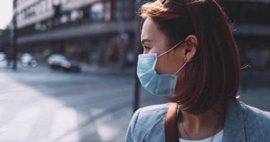 Şehirde koruyucu bir maske takan bir kadın. Yavaş hareket, Gimbal Dengeleyici. Hava kirliliği ve Coronavirus Covid-19 'a karşı maskeli genç bir kadın sokakta dolaşıyor. Şehir Sabahı.
