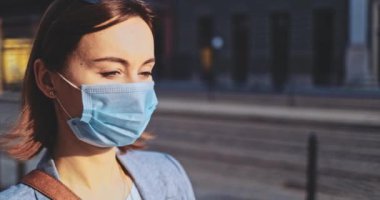 Şehirde koruyucu bir maske takan bir kadının portresi. Yavaş hareketli Gimbal Stabilizer atışı. Hava kirliliği ve Coronavirus covid-19 'a karşı maskeli genç bir kadın caddeyi geçiyor..