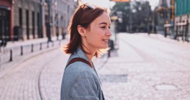Şehirde yürüyen ve kamerayla konuşan genç bir kadın. Yavaş hareket, Gimbal Dengeleyici. İş kadını kameranın arkasındaki biriyle sohbet ediyor. Açık havada iletişim kurmak..