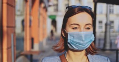Şehirde koruyucu bir maske takan bir kadının portresi. Yavaş hareketli Gimbal Stabilizer atışı. Hava kirliliği ve Coronavirus covid-19 'a karşı maskeli genç bir kadın caddeyi geçiyor..