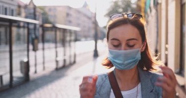 Kadın şehirde nefes almak için koruyucu maskeyi çıkartıyor. Yavaş hareket, Gimbal Dengeleyici. Hava kirliliğine ve Coronavirus Covid-19 'a karşı maskeli bir kız sokakta dolaşıyor..