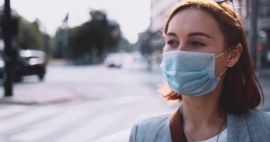 Koruyucu maskeli bir kadın kahve içiyor, şehirde yürüyor. Yavaş bir hareket yap. Genç bayan hava kirliliğine ve Coronavirus covid-19 'a karşı maskesini çıkararak kağıt bardaktan su içiyor..