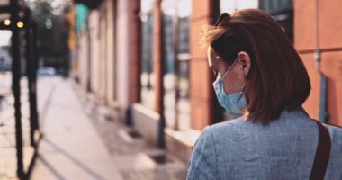 Şehirde koruyucu bir maske takan bir kadın. Yavaş hareket, Gimbal Dengeleyici. Hava kirliliği ve Coronavirus Covid-19 'a karşı maskeli genç bir kadın sokakta dolaşıyor. Şehir Sabahı.