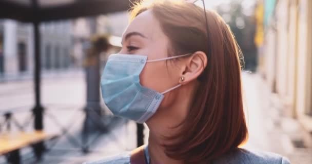 Retrato de una mujer con una máscara protectora caminando por la ciudad. Movimiento lento Gimbal estabilizador disparo. Mujer joven en una máscara facial contra la contaminación del aire y coronavirus covid-19, cruzando la calle. — Vídeo de stock