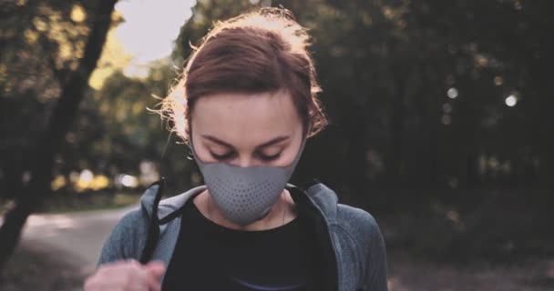 O femeie care aleargă de pe o mască de protecție pentru a respira în parcul însorit din oraș care face exerciții în aer liber. Gimbal STABILIZED, SLOW MOTION. Femeie într-o mască de față împotriva poluării aerului și Covid19 dimineață Jog — Videoclip de stoc