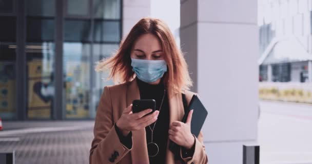 Деловая женщина в защитной маске использует смартфон ходить по городу. СЛОУ МИЙОН Гимбал. Женщина-предприниматель в медицинской маске против загрязнения воздуха и коронавируса Covid19 — стоковое видео