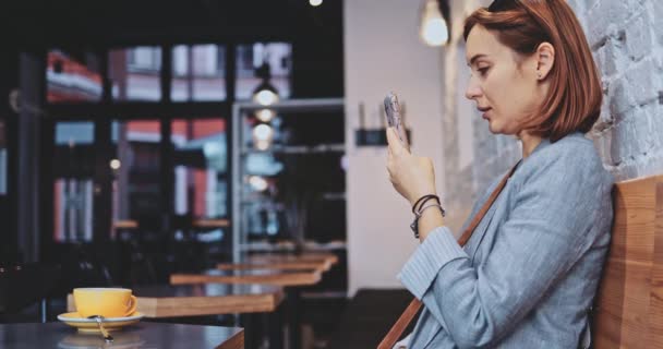 Junge Frau benutzt Smartphone in einem Coffeeshop Slow Motion, Stabilisator. Geschäftsfrau dreht Videos für soziale Medien in einem Café, kommuniziert, baut persönliche Marke auf, online. Technologie im Leben — Stockvideo