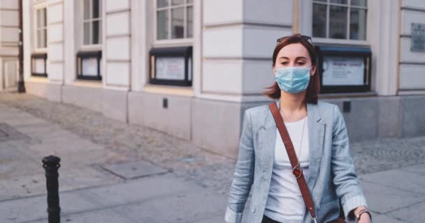 Жінка носить захисну маску, яка ходить по місту. SLOW MOTION, Gimbal Stabilizer. Молода жінка в масці перед лицем проти забруднення повітря і коронавірусу Ковід-19, на вулиці і навколо. Міський ранок. — стокове відео