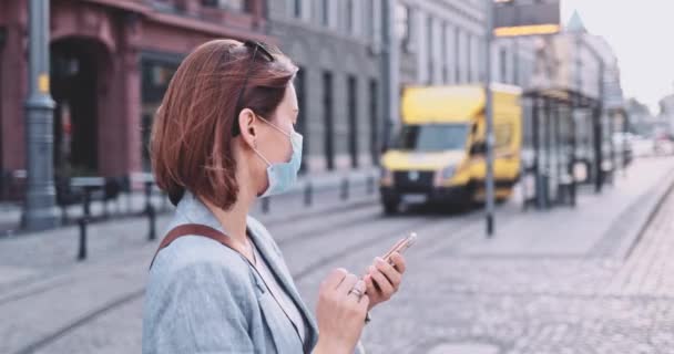 Woman Wearing A Protective Mask Walking In The City, Using Smartphone. SLOW MOTION, Gimbal Stabilizer. Young Female in face mask against air pollution and coronavirus Covid-19. Urban Morning. — Stock Video