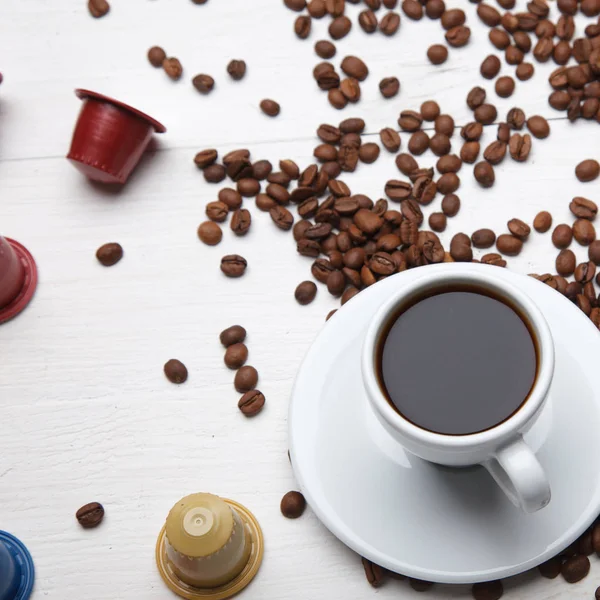 Coffee concept. Full cup of coffee with colorful capsules for coffee machine, beans, on white table top view