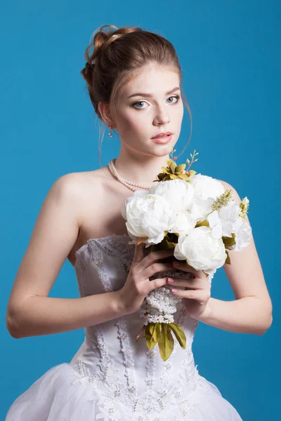 Young and pretty bride with flowers studio shot isolated on blue