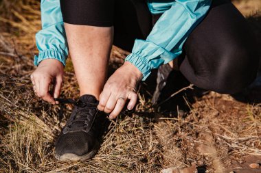 Yürüyüş yapan bir kız spor ayakkabılarını bağlıyor.