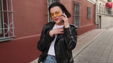 Milenyum kadını sokakta yürüyor telefonda güzel güzel konuşuyor ve gülümsüyor, sevgilisi ya da arkadaşıyla sohbet etmekten hoşlanıyor. Gülümseyen kadın telefonla konuşuyor..