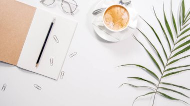 Flat lay white minimalistic office work space desk with copy space background. Work place with cappuccino cup coffee, notebook, glasses and palm branch. clipart