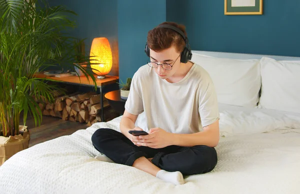 Evde, yatakta otururken en sevdiği müziği telefon ve kulaklıkla dinleyen genç bir adam. Öğrenciler en iyi şarkıları ve hitleri, müzik listesini ve akıllı telefondan radyoyu severler. Dil öğren.