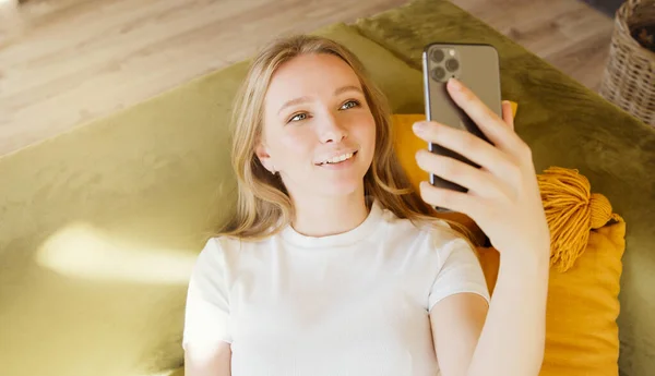 Young woman making video chat online or making photo selfie on mobile phone at home. Talking over video call conference  recording vlog.