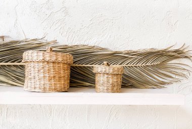Hasır, beyaz raflarda kuru palmiye yapraklarıyla dekoratif sepetler. Minimalist İskandinav iç mimarisi. 