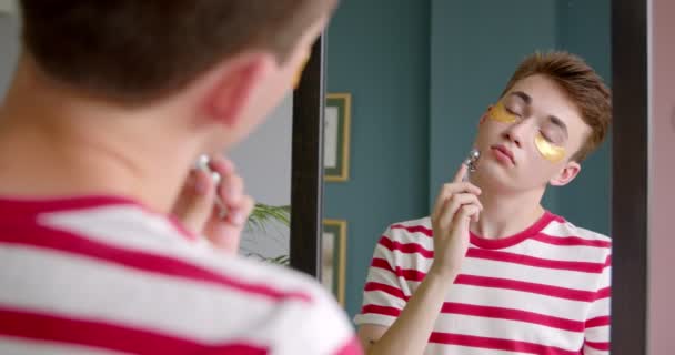 Unge Man Gör Skönhetsrutin Framför Spegeln Massera Ansiktet Med Rullmassager — Stockvideo