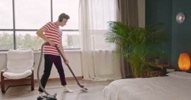 Genç adam evi temizlerken ve süpürgeyle dans ederken eğleniyor. Erkek temizliği ve ev işi, etrafta dolaşmak ve kulaklıkla komik müzik dinlemek..