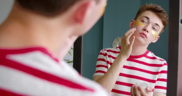 鏡の中に顔に保湿クリームを塗る若い男 ホームスキンケア 健康的な治療の概念 — ストック動画