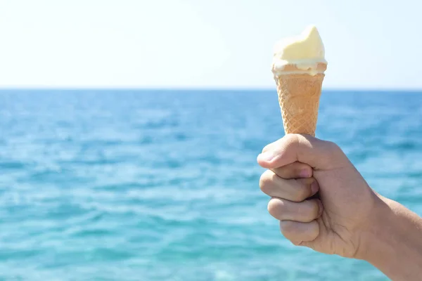 Child hand holding ice cream opposite blue sea — Stock Photo, Image
