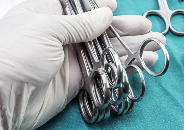 Surgeon working in operating room, hands with gloves holding scissors sutures, conceptual image, composicon horizontal