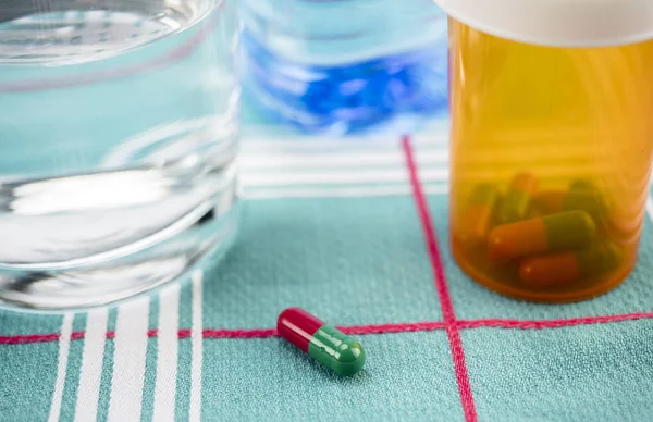 Medicatie tijdens het ontbijt, capsules naast een glas water, conceptueel beeld, horizontale samenstelling — Stockfoto