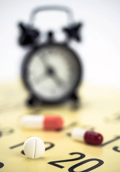 Pills on a calendar next to a clock, conceptual image — Stock Photo, Image