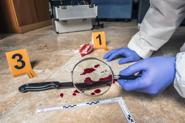 Ekspert Policji badający szkłem powiększającym nóż z krwią na miejscu zbrodni, konceptualny obraz — Zdjęcie stockowe