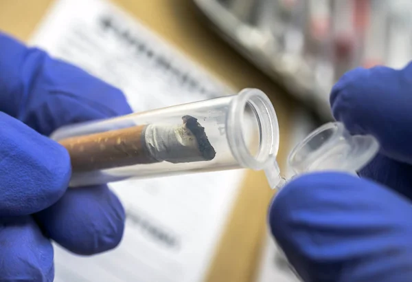 Polícia especialista examina uma ponta de cigarro em laboratório balístico, imagem conceitual — Fotografia de Stock