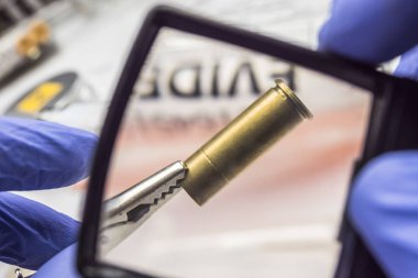 Uzman polis, laboratuarda bir kurşun kapağını büyüteçle inceliyor.