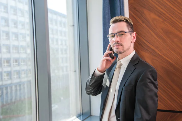 manager talking on the phone / the manager talking on the phone in the office, in front of the window